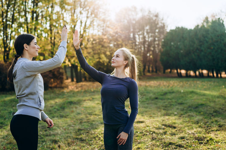 Two girls in the park are exercising and clapping their hands.