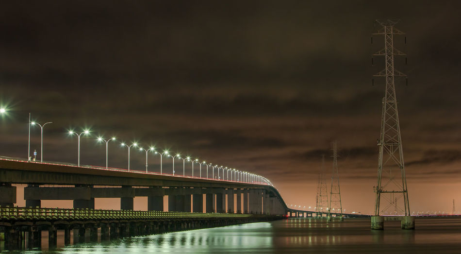 Illuminated san mateo-hayward bridge over river against cloudy sky at night