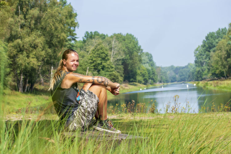 Full length of woman sitting on grass by lake