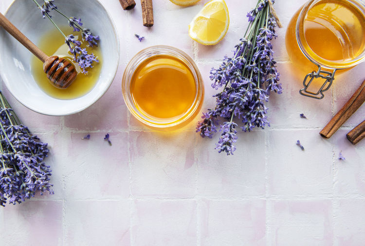 Jars and bowl with honey and fresh lavender flowers on a pink tile background
