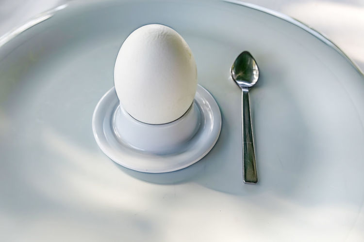 Close up egg in eggcup with little spoon on white plate