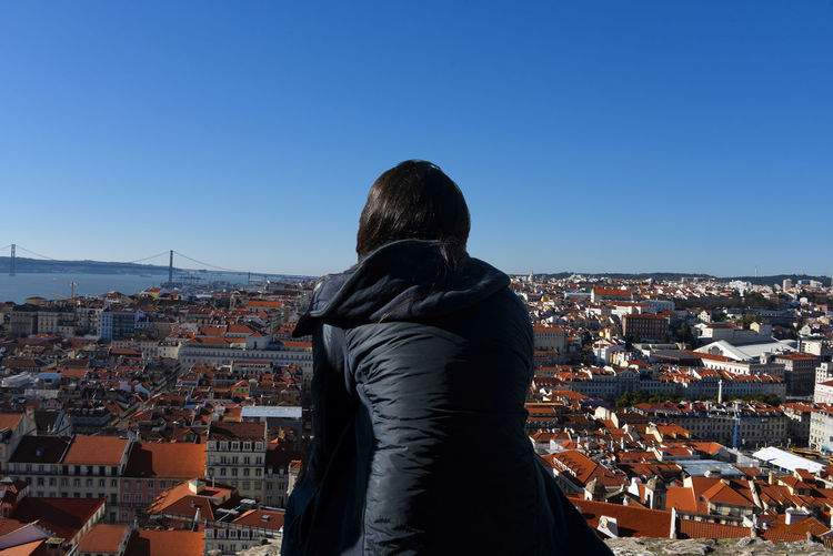 Rear view of woman standing against cityscape against clear blue sky
