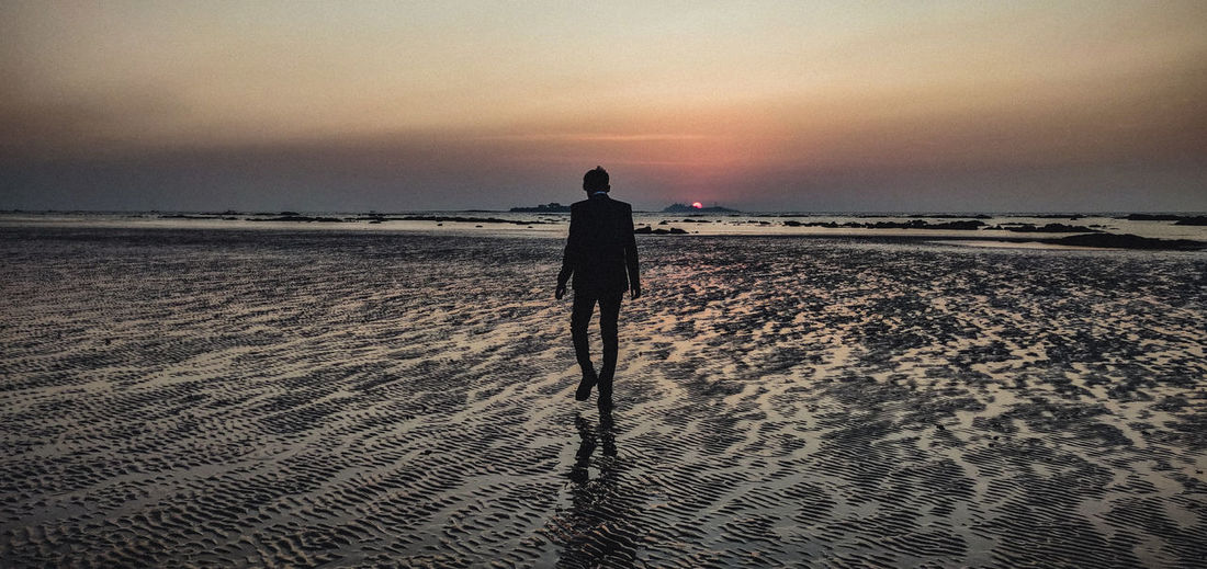 Rear view of man walking on a beach during sunset, towards oblivion.