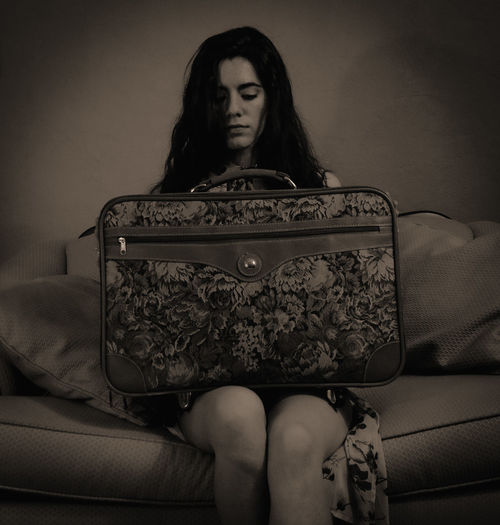 Young woman with suit case sitting on sofa at home