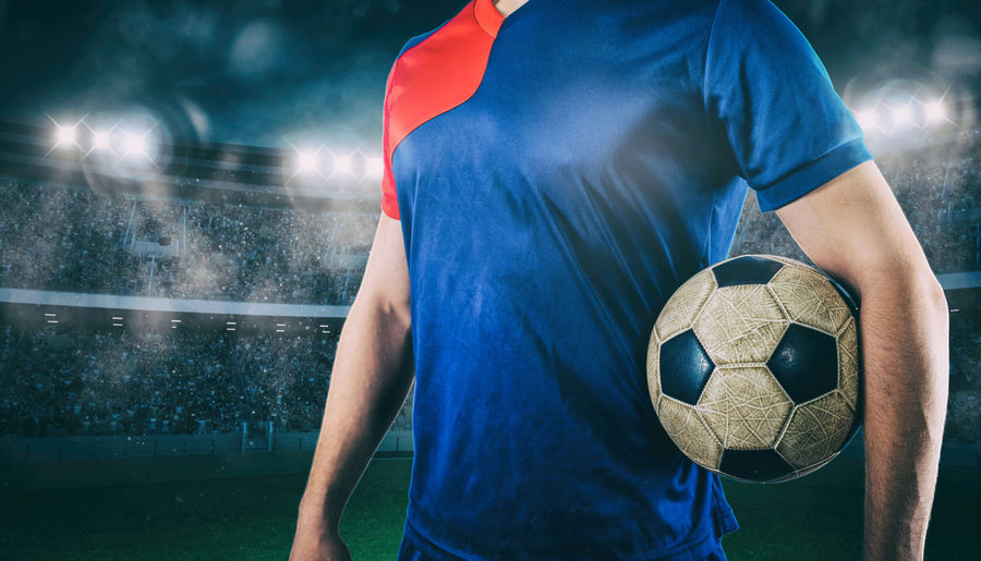 Midsection of man holding soccer ball on field
