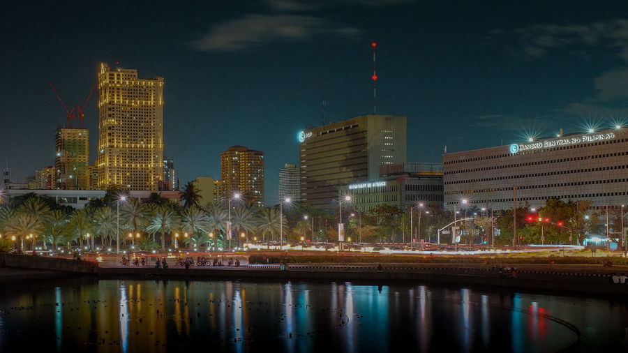 Illuminated buildings by river against sky in city at night
