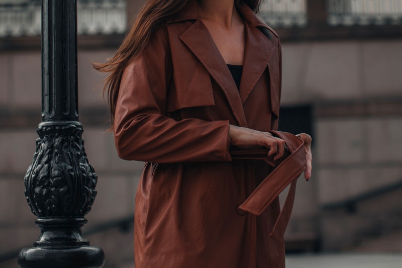 Cropped stylish young woman in fashionable long brown leather coat. pretty elegant girl model posing