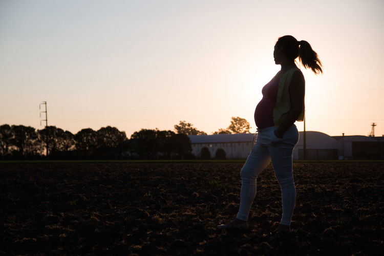 Full length of pregnant woman standing on field against sky during sunset