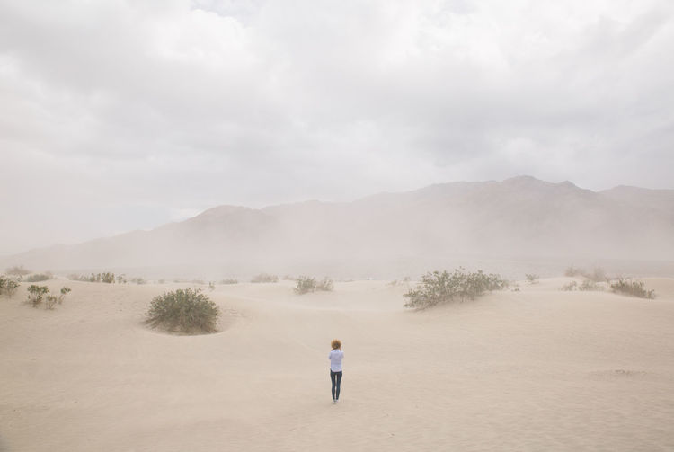 Rear view of woman standing at death valley against sky during sandstorm
