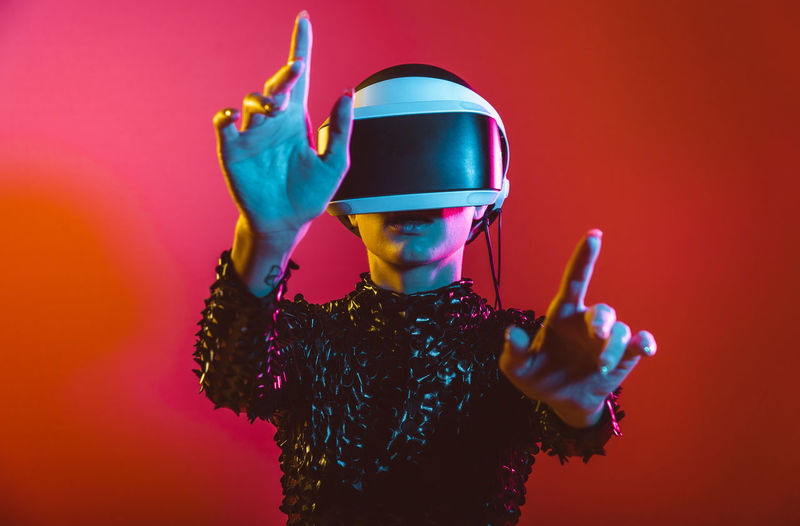 Young woman with shaved head wearing virtual reality glasses against pink background
