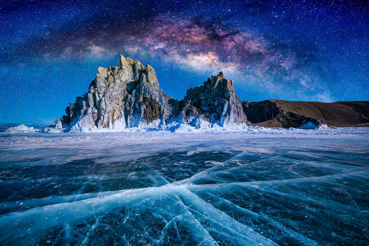 Rock formations by frozen sea against blue sky