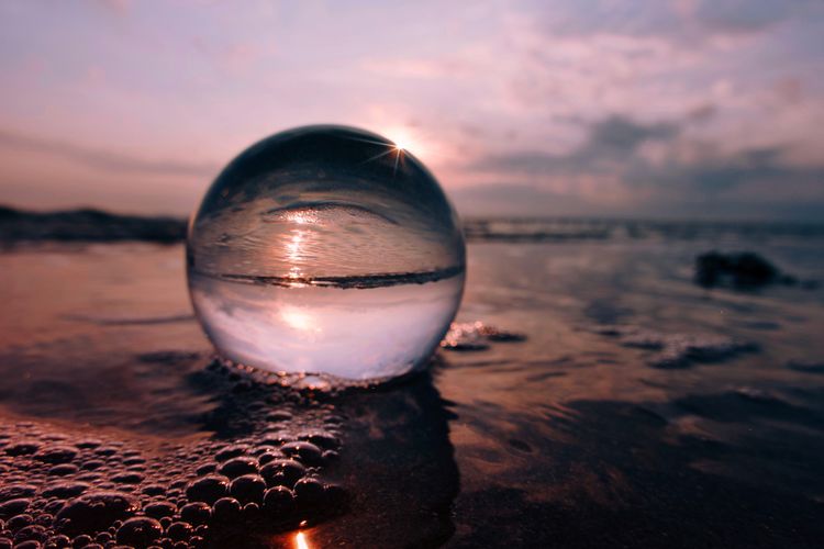 Close-up of crystal ball on beach against sky during sunset