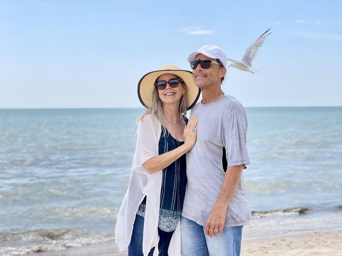 Happy senior couple enjoying being together on the beach as seagull flys by against water and sky.