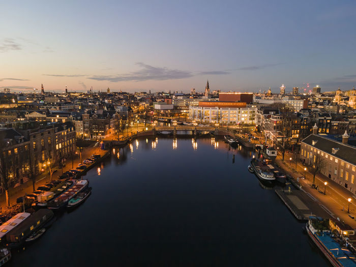 High angle view of illuminated buildings by river against sky in amsterdam