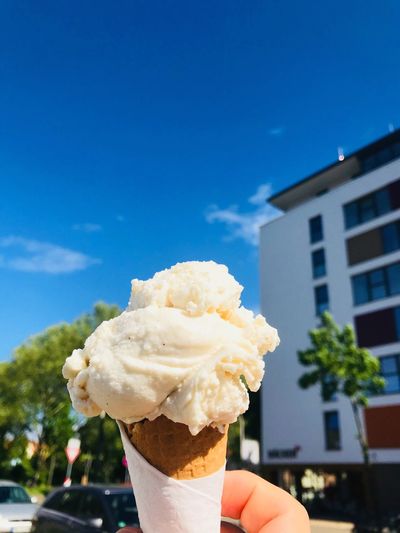 Cropped hand holding ice cream cone against blue sky