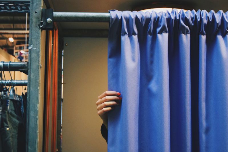 Cropped hand of woman closing blue curtain of changing room