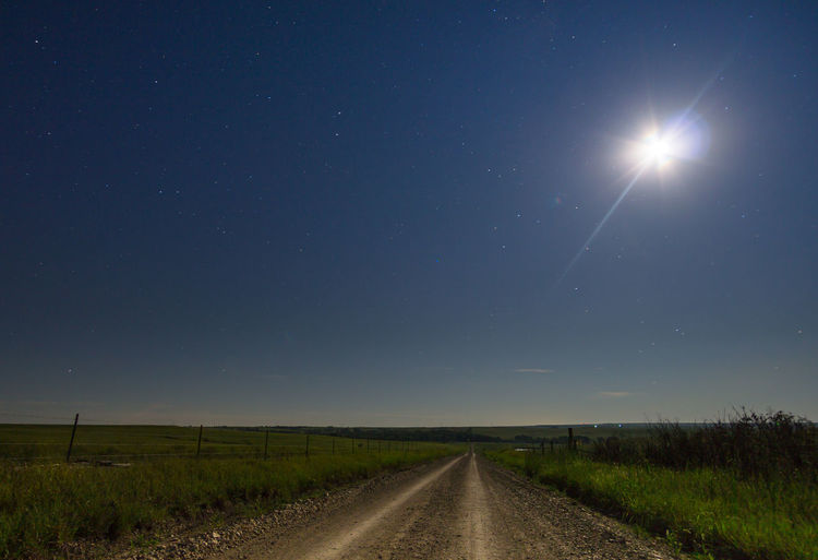 Empty road amidst landscape against sky at night