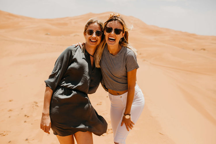 Cheerful friends standing on sand at desert against sky