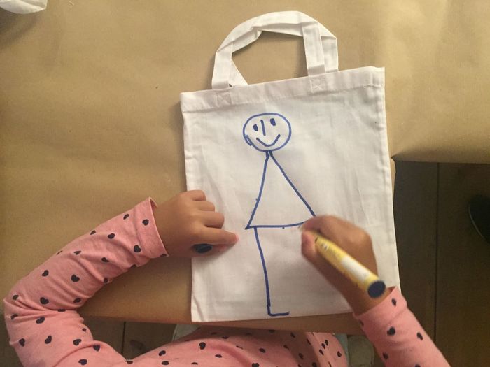 Midsection of kid drawing on white bag at home
