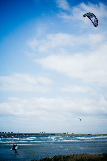 Person kiteboarding at beach against cloudy sky