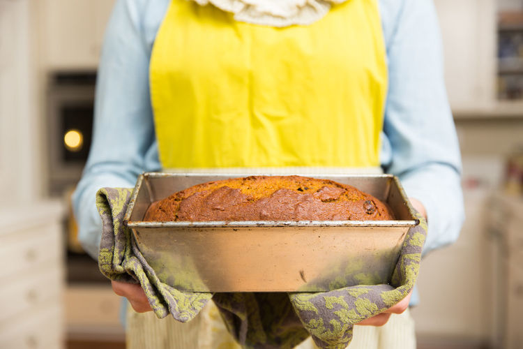 Midsection of chef holding pumpkin bread loaf in container