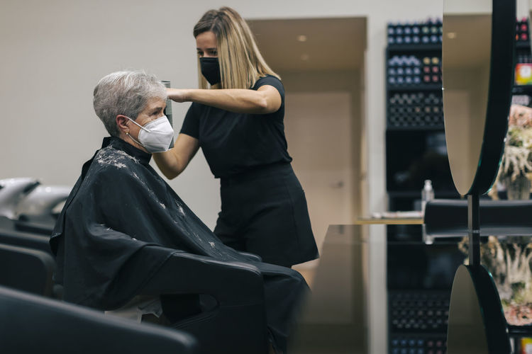 Female hairdresser with face mask cutting customer's hair in salon