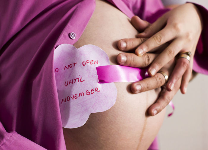 Cropped image of woman and man holding pregnant abdomen with text 