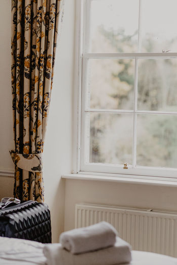 Suitcase placed near window decorated with floral curtain in light hotel room