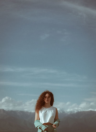 Portrait of woman with curly hair standing against sky