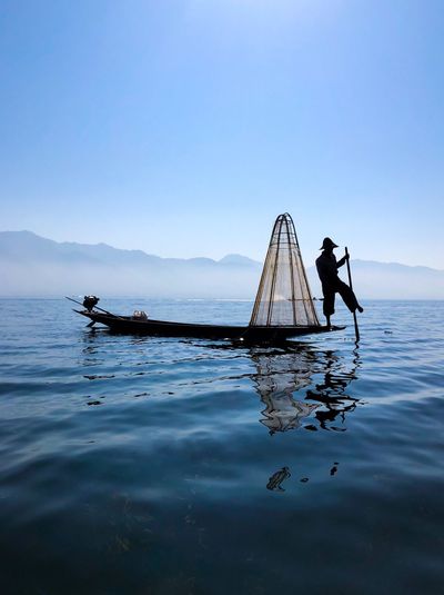 Fisherman on boat in lake against sky