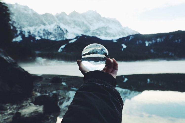Rear view of man holding crystal ball against snowcapped mountains