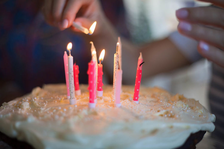 Close-up of hand igniting candles on birthday cake at table
