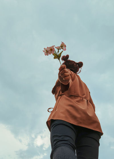 Low angle view of person holding flowering plant against sky