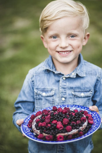 Portrait of smiling boy holding berry tart in garden