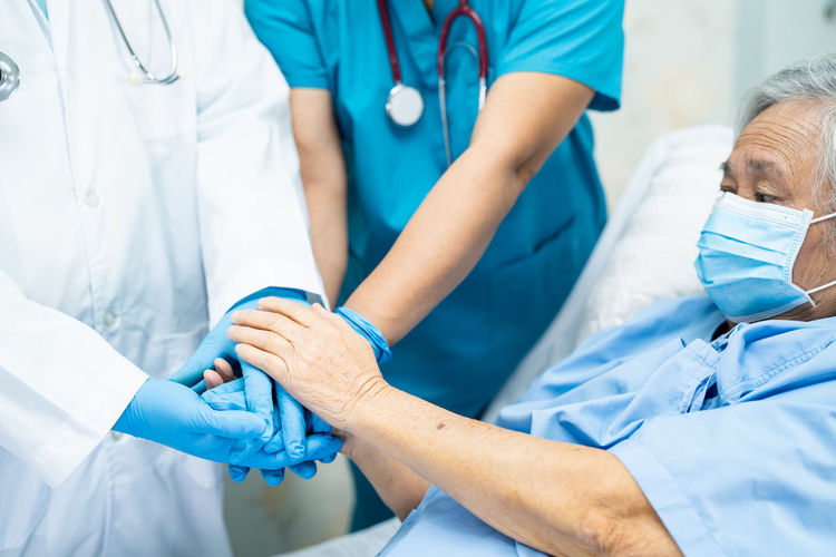 Midsection of doctors holding patient hands in hospital
