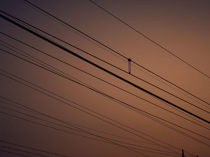 Low angle view of power cables against sky during sunset