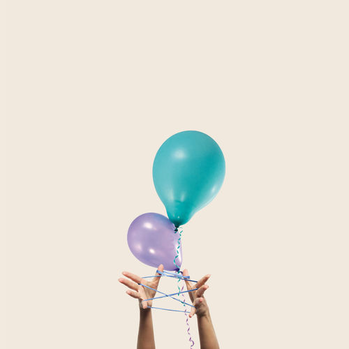 Close-up of hand holding balloons against white background