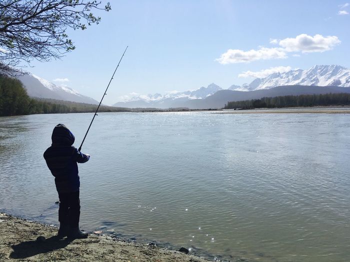 Boy fishing in lake against sky in alaska