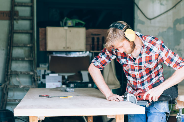 carpenter working on wood in his workshop Craftsman Workshop Adult Art And Craft Business Carpenter Carpenter Tools Casual Clothing Concentration Craft Design Professional Hobby Indoors Males Men Occupation One Person Real People Standing Table Technology Woodworking Workbench Working Workshop