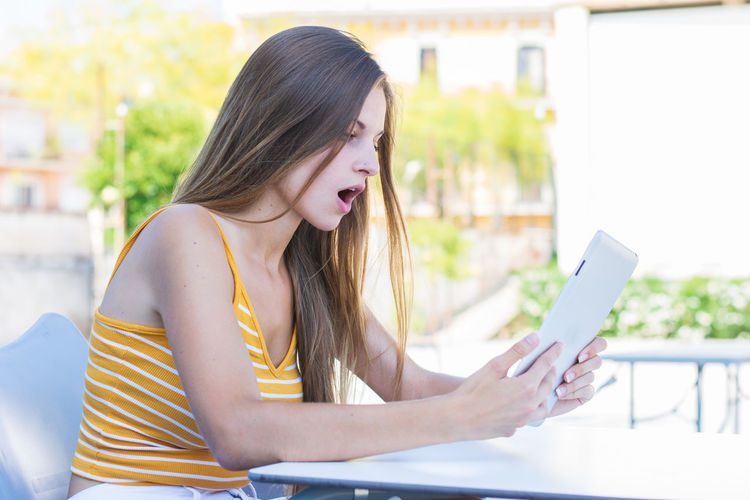 Shocked girl using mobile phone while sitting on table outdoors