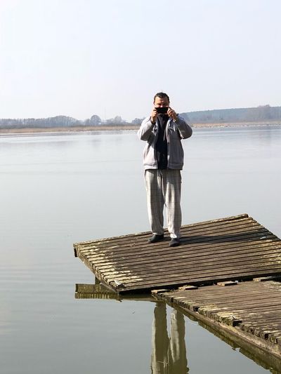 Man photographing while standing on pier over lake against sky