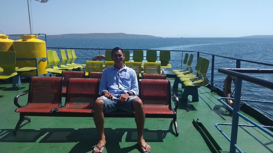 Full length of man sitting on seat against sea
