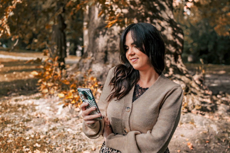 Young woman using mobile phone, autumn, fall, happy, smiling.