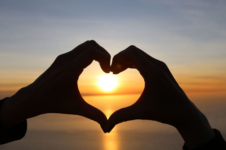 Cropped image of silhouette hands forming heart against sea during sunset