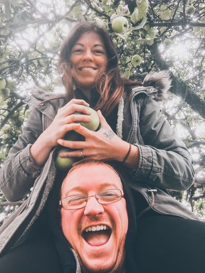 Portrait of smiling woman holding fruits over man against tree