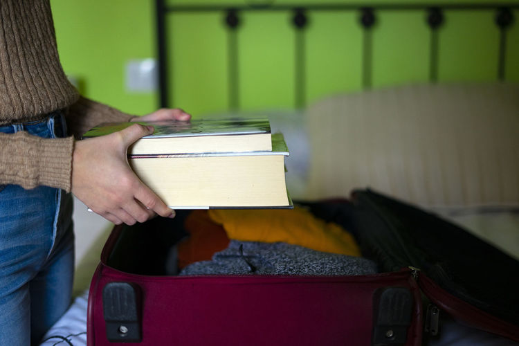 Woman traveler and reader putting books in her travel suitcase.