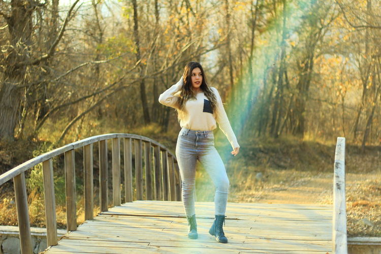 Young woman standing on footbridge at forest during autumn