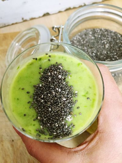 Cropped hand holding green smoothie glass and chia seeds