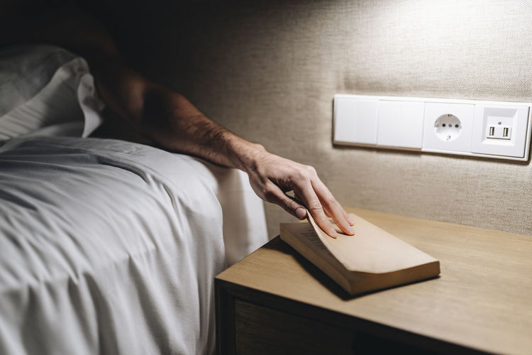 Man keeping book on table by bed