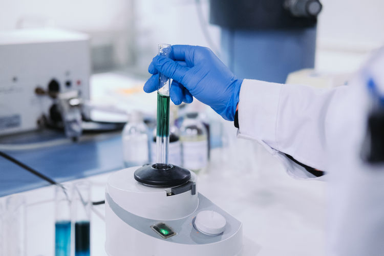 Crop view of hands of worker in rubber gloves and uniform using centrifuge machine for medical research in laboratory